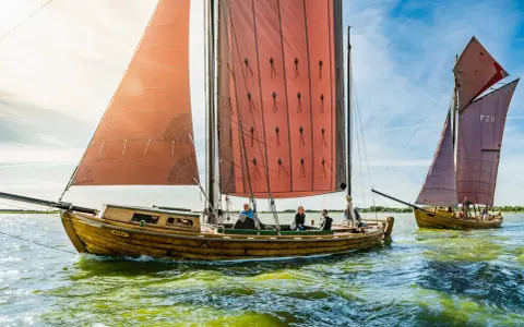 Zeesboot "Bill" segelt bei Ahrenshoop mit roten Segeln. Ein zweites Boot folgt.