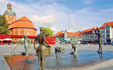 Bronzefiguren am Brunnen in Ribnitz-Damgarten, mit Kirche und Fachwerkhäusern im Hintergrund. Ein Ort, der an Bernstein erinnert.