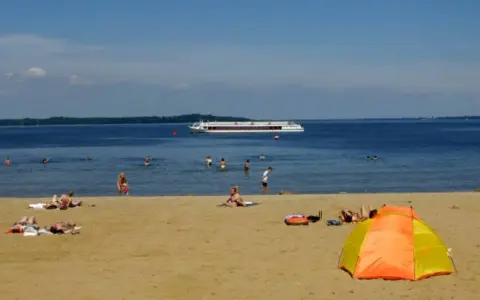 Sonne, Sand und ein Schiff auf dem Wasser – ein entspannter Tag am Schweriner Strand mit Badegästen und einer bunten Strandmuschel.