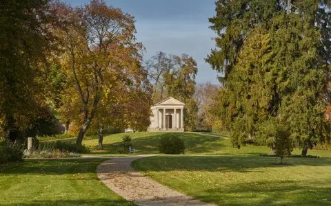 Herbstlicher Spaziergang im Schlossgarten Neustrelitz. Ein Weg führt zu einem antiken Mausoleum, umgeben von bunten Bäumen.