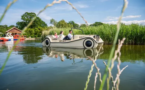Familie genießt eine Fahrt mit einem Auto-Boot von Kiki's Bootsverleih auf einem ruhigen See, umgeben von üppigem Grün.