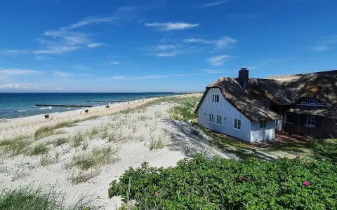Ein reetgedecktes Haus am Strand von Ahrenshoop, mit Blick auf die Ostsee und den Sandstrand.