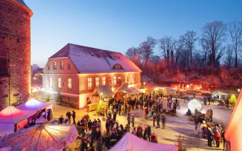 Belebter weihnachtsmarkt plau am see vor historischer Kulisse mit beleuchteten Buden und vielen Besuchern.