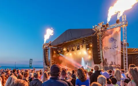 Feuerfontänen lodern bei Konzerten an der Ostsee. Eine Menschenmenge feiert am Strand zu elektronischer Musik.