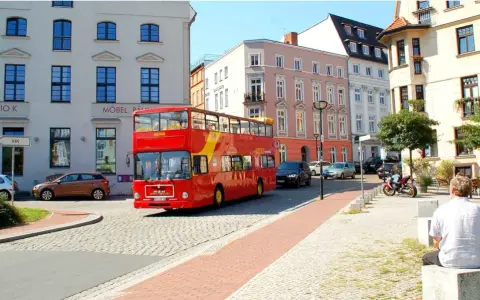 Roter Doppeldeckerbus für eine Stadtrundfahrt in Rostock fährt durch eine Gasse mit historischen Gebäuden.