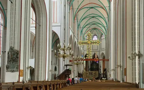 Imposanter Innenraum des Schweriner Doms mit Holzbänken, einem großen goldenen Kreuz und grünen Gewölben.