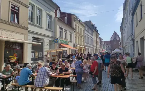 Menschen genießen ein Fest vor dem Kulturhaus Teterow. Viele sitzen an Tischen, essen und unterhalten sich.