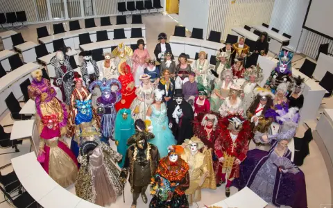 Eine Gruppe in prächtigen Kostümen und Masken, die an venezianische Tage in Schwerin erinnert, versammelt sich in einem modernen Sitzungssaal.