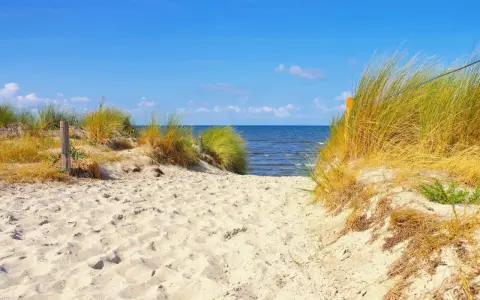 Sandiger Weg durch Dünen zum Strand auf der Insel Poel. Das Meer glitzert im blauen Himmel.
