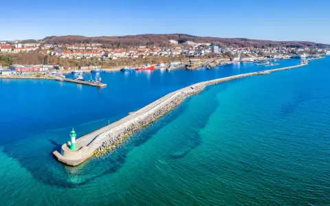 Leuchtturm am Ende einer Mole, die in das klare Wasser vor Sassnitz führt. Boote und die Stadt im Hintergrund.