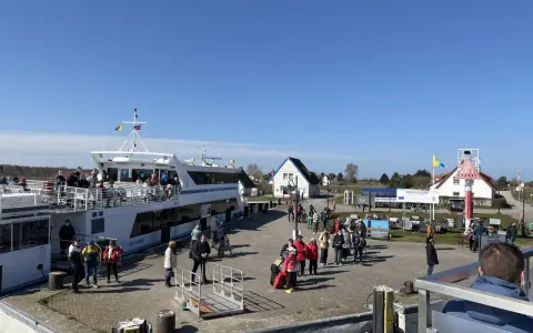 Menschen warten am Kai in Neuendorf auf Hiddensee auf die Fähre. Ein großes Ausflugsschiff liegt bereit.