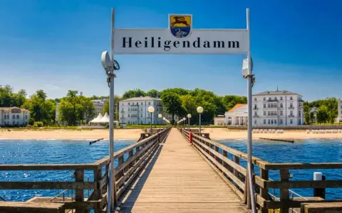 Holzsteg führt zum Heiligendamm Strand mit weißen Gebäuden und blauem Himmel.