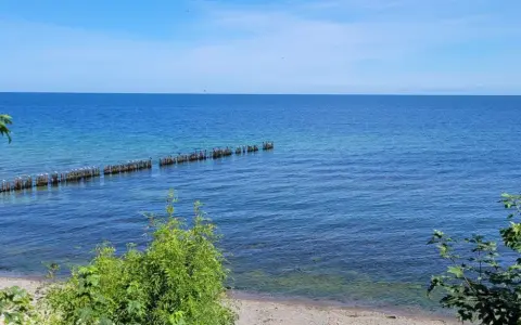 Ein ruhiger Tag am glühenden Strandpromenade. Das Meer ist ruhig, mit einer Reihe von Holzpfählen, auf denen Vögel sitzen.