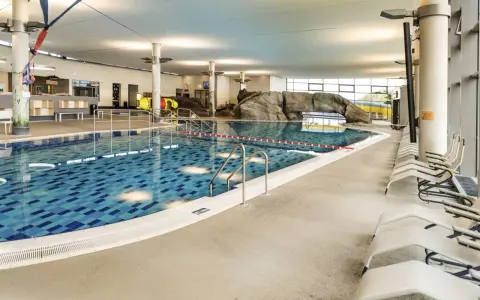 Ein großes Schwimmbecken mit blauen Kacheln und einer Felswand lädt zum Badespaß ein. Hier ist das perfekte Erlebnisbad Ostsee für die ganze Familie.