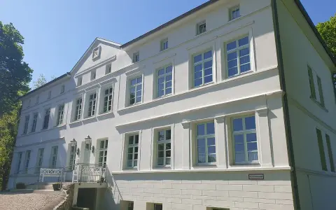 Das Herrenhaus Blengow, ein weißes Gebäude mit vielen Fenstern, steht unter blauem Himmel.