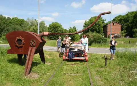 Eine Gruppe von Menschen auf einer Draisine Dargun, neben einer rostigen Skulptur.