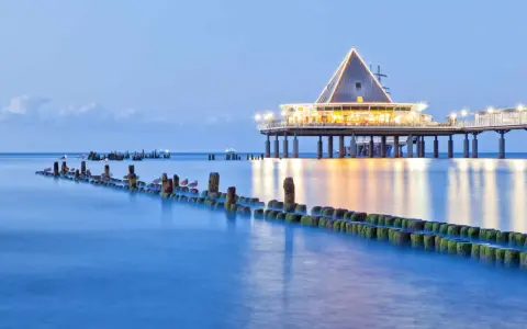 Ein beleuchteter Pier mit Restaurant und Wellenbrechern im Meer. Perfekt für einen Heringsdorf Urlaub.