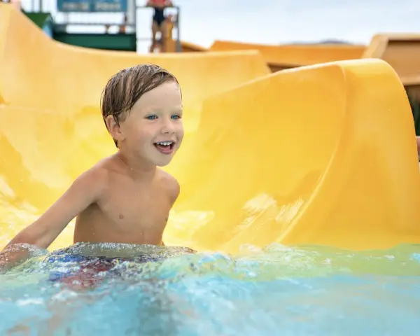 Ein Junge mit blauen Augen lacht fröhlich im Wasser der Wasserrutsche im Heidebad Torgelow.