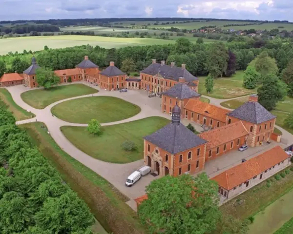 Luftaufnahme von Schloss Bothmer, einem barocken Anwesen mit roten Ziegelgebäuden, umgeben von grünen Gärten und Feldern.