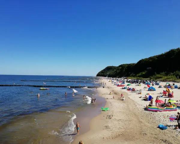 Sonniger Tag am Strand Koserow mit vielen Badegästen, bunten Sonnenschirmen und spielenden Kindern im flachen Wasser.
