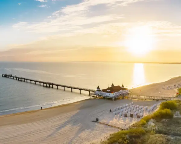 Sonnenuntergang am Ostsee Strand mit langer Seebrücke und Strandkörben.
