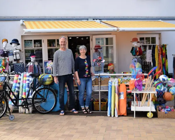 Ein Paar vor einem Laden mit Strandartikeln. Sie sind bereit, juliusruh einkaufen zu gehen und haben alles für einen schönen Tag am Meer.