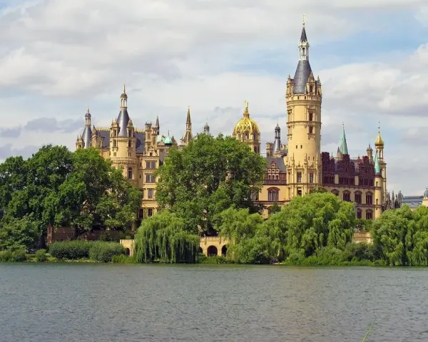 Ein märchenhaftes Schloss mit vielen Türmen und goldenen Kuppeln, umgeben von grünen Bäumen, spiegelt sich im Wasser. Ein gut gremmelin-artiger Anblick.