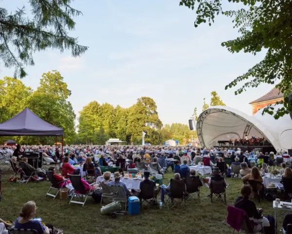 Großes Publikum bei einem Open-Air-Konzert im Rahmen eines **Festivals Mecklenburg-Vorpommern**. Eine Bühne mit Orchester, viele Sitzende auf Rasenflächen.