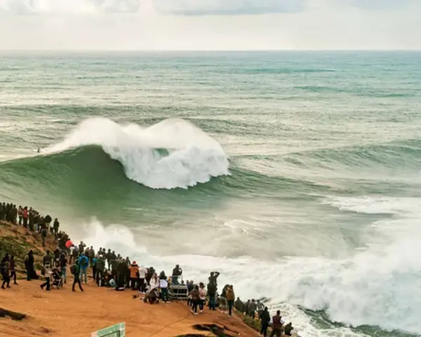 Riesige Welle bricht vor Zuschauern am mole strand. Ein Surfer reitet die Welle.