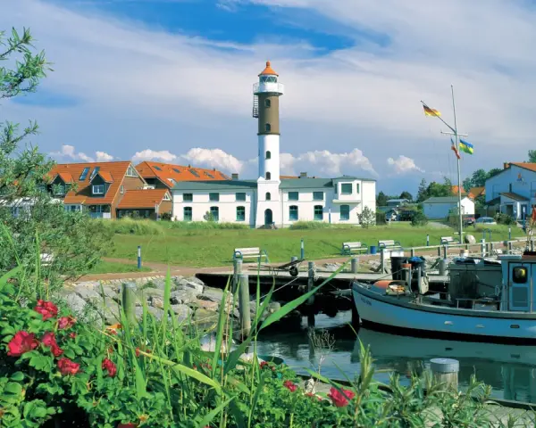 Idyllischer Hafen mit Leuchtturm auf Insel Poel, ein echter Geheimtipp. Boote liegen im Wasser, rote Rosen blühen.