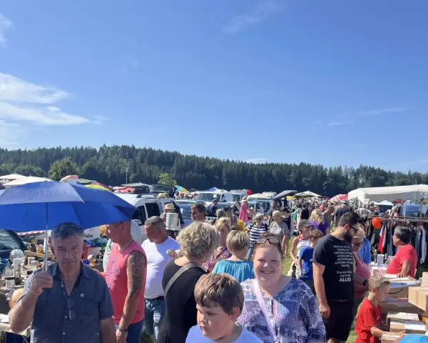 Buntes Treiben auf dem Flohmarkt Sellin. Menschen stöbern an Ständen unter blauem Himmel, im Hintergrund ein Wald.
