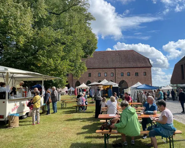 Sommerliche Zarrentin Veranstaltungen: Menschen genießen ein Fest mit Ständen und Sitzgelegenheiten im Freien vor historischen Gebäuden.