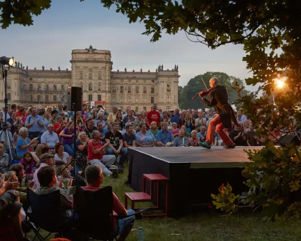 Ein Geiger spielt auf einer Bühne vor einem Schloss, während ein Publikum zusieht. Ein schönes Beispiel für Veranstaltungen an der Ostsee.