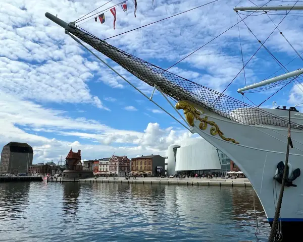 Die Gorch Fock in Stralsund, ein stolzes Segelschiff, liegt vor einer malerischen Kulisse mit historischen Gebäuden und moderner Architektur am Hafen.