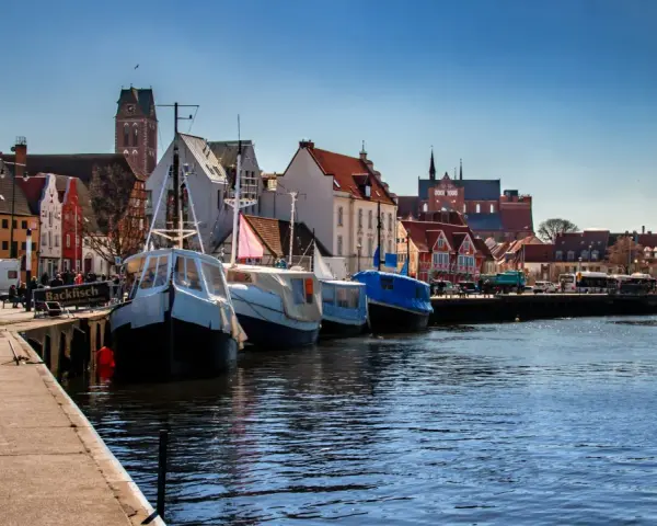 Boote liegen im **Wismar Hafen** vor bunten Häusern. Ein Schild wirbt für "Backfisch".