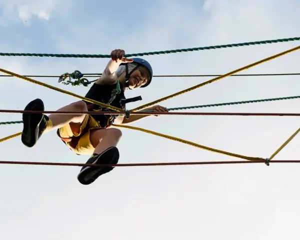 Ein Kind balanciert im Kletterwald Born über Seile. Mit Helm und Sicherung meistert es den Parcours.