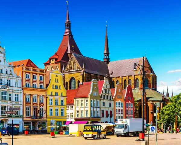 Bunte Giebelhäuser und die Marienkirche prägen das Bild der Rostocker Innenstadt. Ein sonniger Tag auf dem Platz.