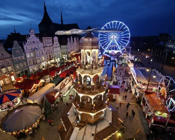 Ein beleuchteter Weihnachtsmarkt Mecklenburgische Seenplatte mit Riesenrad, Pyramide und Buden.