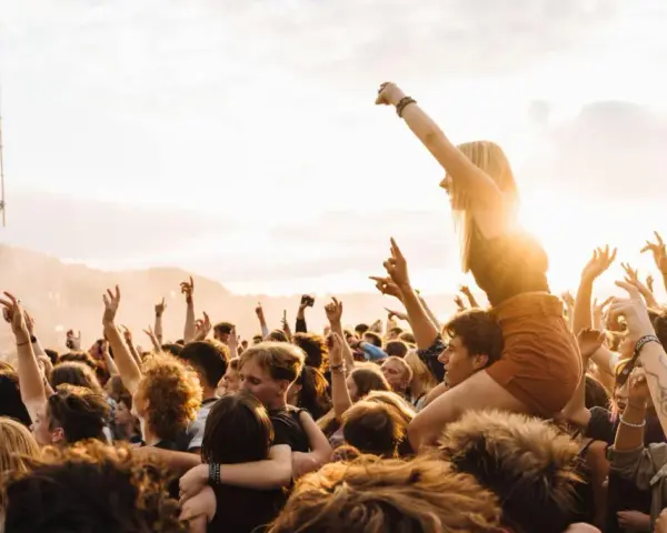 Menschen jubeln auf einem Festival in Rostock. Eine Frau sitzt auf den Schultern eines anderen Besuchers, während die Sonne untergeht.