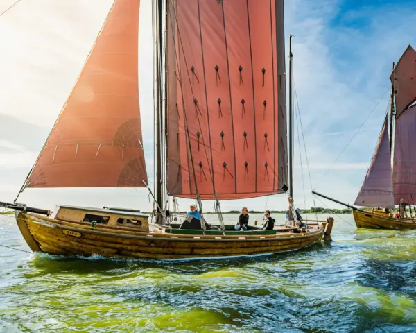 Zeesboot "Bill" segelt bei Ahrenshoop mit roten Segeln. Ein zweites Boot folgt.