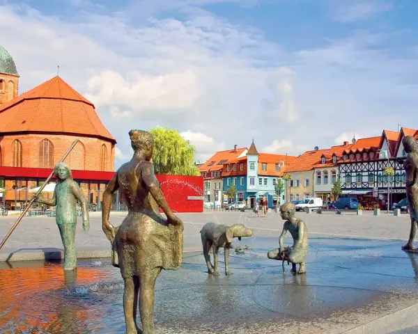 Bronzefiguren am Brunnen in Ribnitz-Damgarten, mit Kirche und Fachwerkhäusern im Hintergrund. Ein Ort, der an Bernstein erinnert.