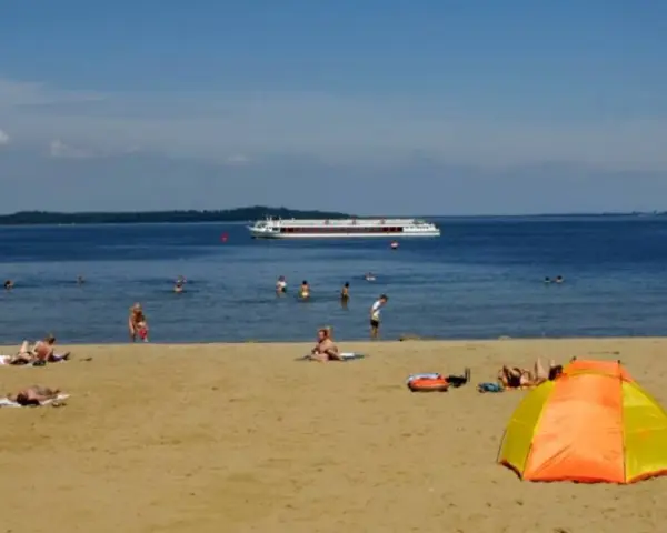 Sonne, Sand und ein Schiff auf dem Wasser – ein entspannter Tag am Schweriner Strand mit Badegästen und einer bunten Strandmuschel.