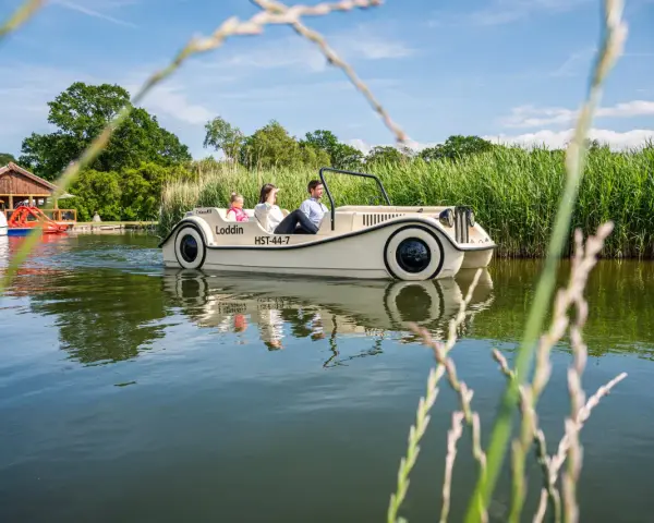 Familie genießt eine Fahrt mit einem Auto-Boot von Kiki's Bootsverleih auf einem ruhigen See, umgeben von üppigem Grün.