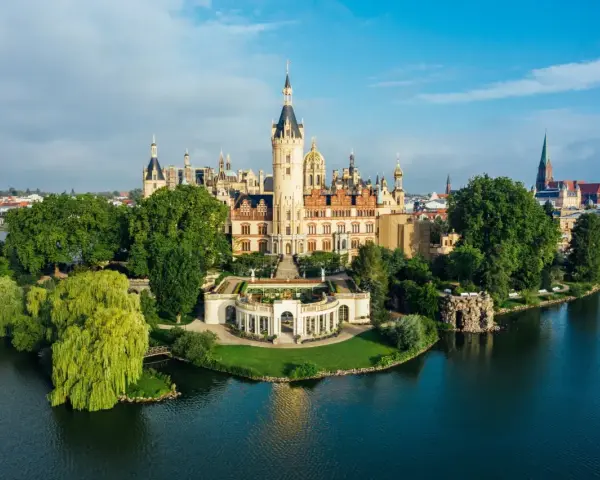 Schweriner Schloss auf einer Insel, umgeben von Wasser und grünen Bäumen. Ein Märchenschloss, das zu den Schwerin Geheimtipps zählt.