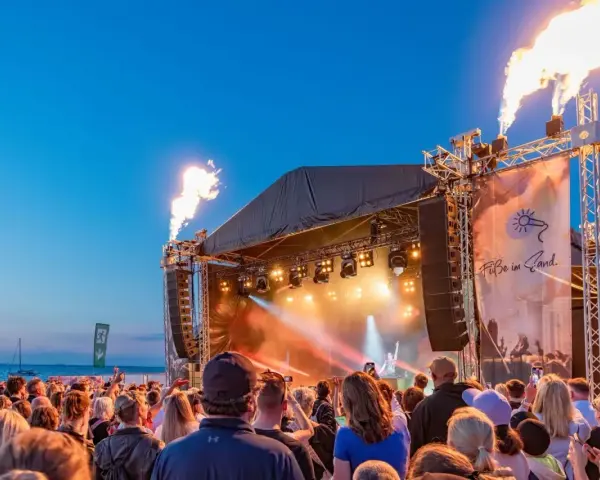 Feuerfontänen lodern bei Konzerten an der Ostsee. Eine Menschenmenge feiert am Strand zu elektronischer Musik.
