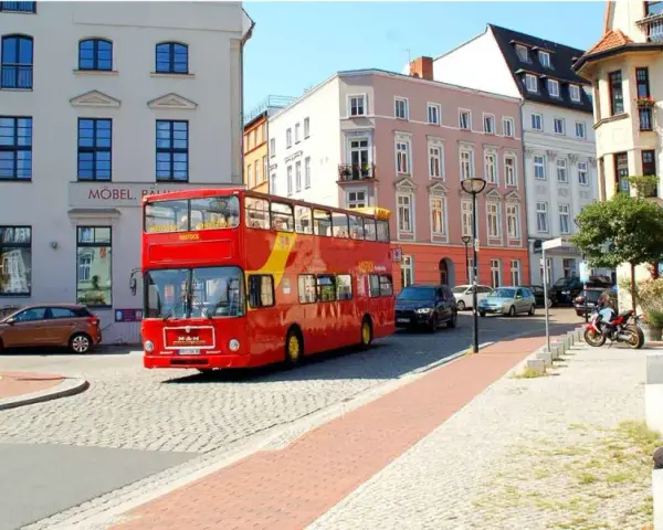 Roter Doppeldeckerbus für eine Stadtrundfahrt in Rostock fährt durch eine Gasse mit historischen Gebäuden.