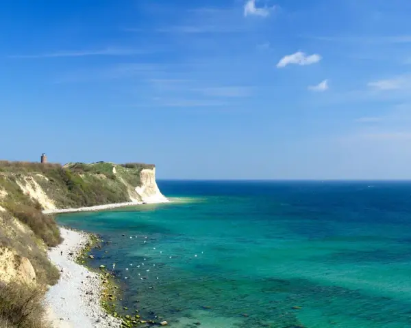 Türkisblaues Meer und Kreidefelsen am Kap Arkona. Ein Leuchtturm wacht über die Küste.