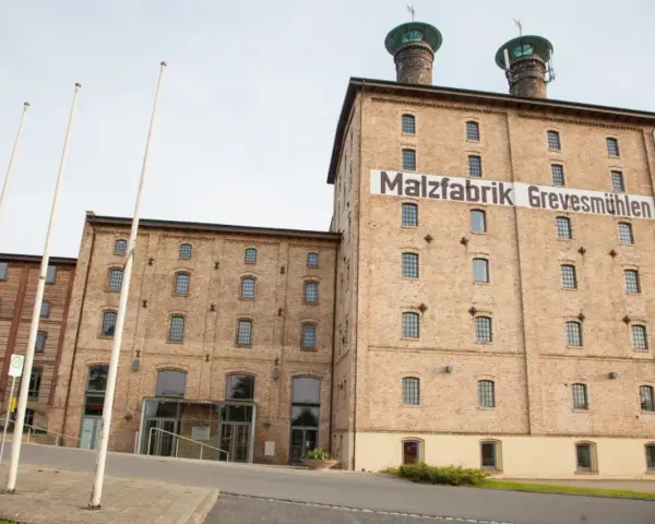 Die imposante Malzfabrik Grevesmühlen, ein Backsteingebäude mit markanten Türmen, steht im hellen Tageslicht.