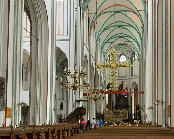 Imposanter Innenraum des Schweriner Doms mit Holzbänken, einem großen goldenen Kreuz und grünen Gewölben.