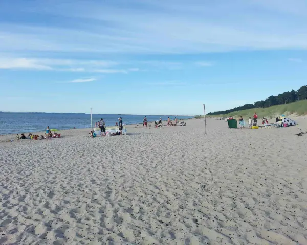 Menschen entspannen sich am sonnigen Lubmin Strand. Das Meer glitzert, der Himmel ist blau mit leichten Wolken.